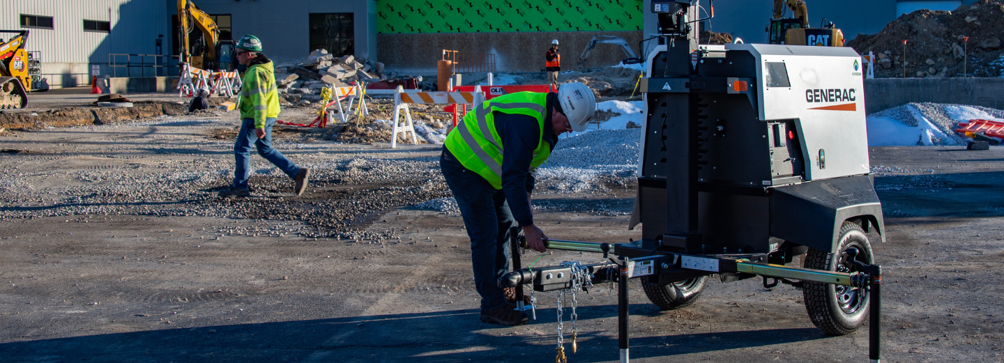 photo of a service technician on an outdoor construction site setting up the base of a Generac light tower aligning to the light tower owners manual